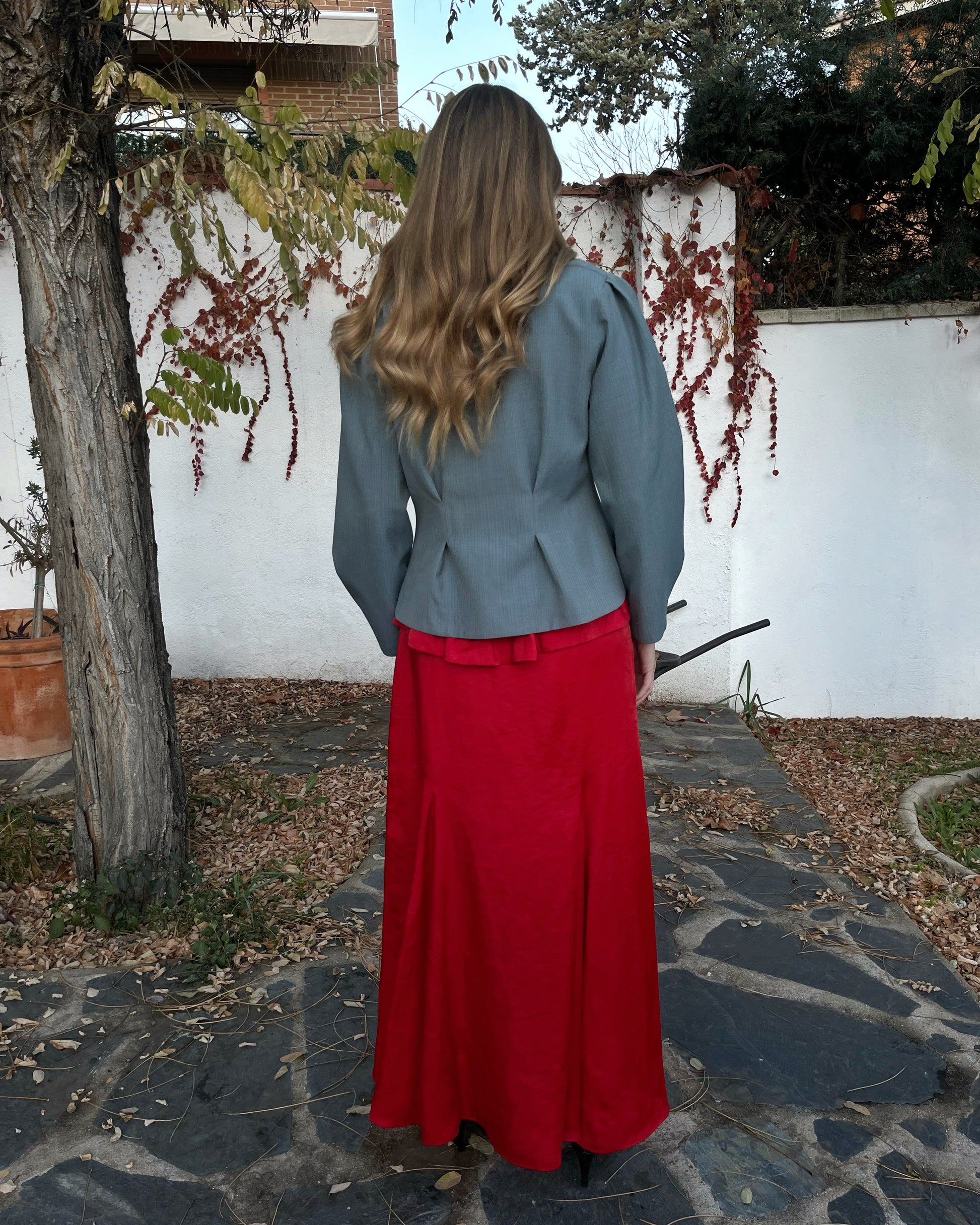 Chaqueta azul de mujer con rayas a tono y pliegues entallados; vista trasera elegante en jardín.