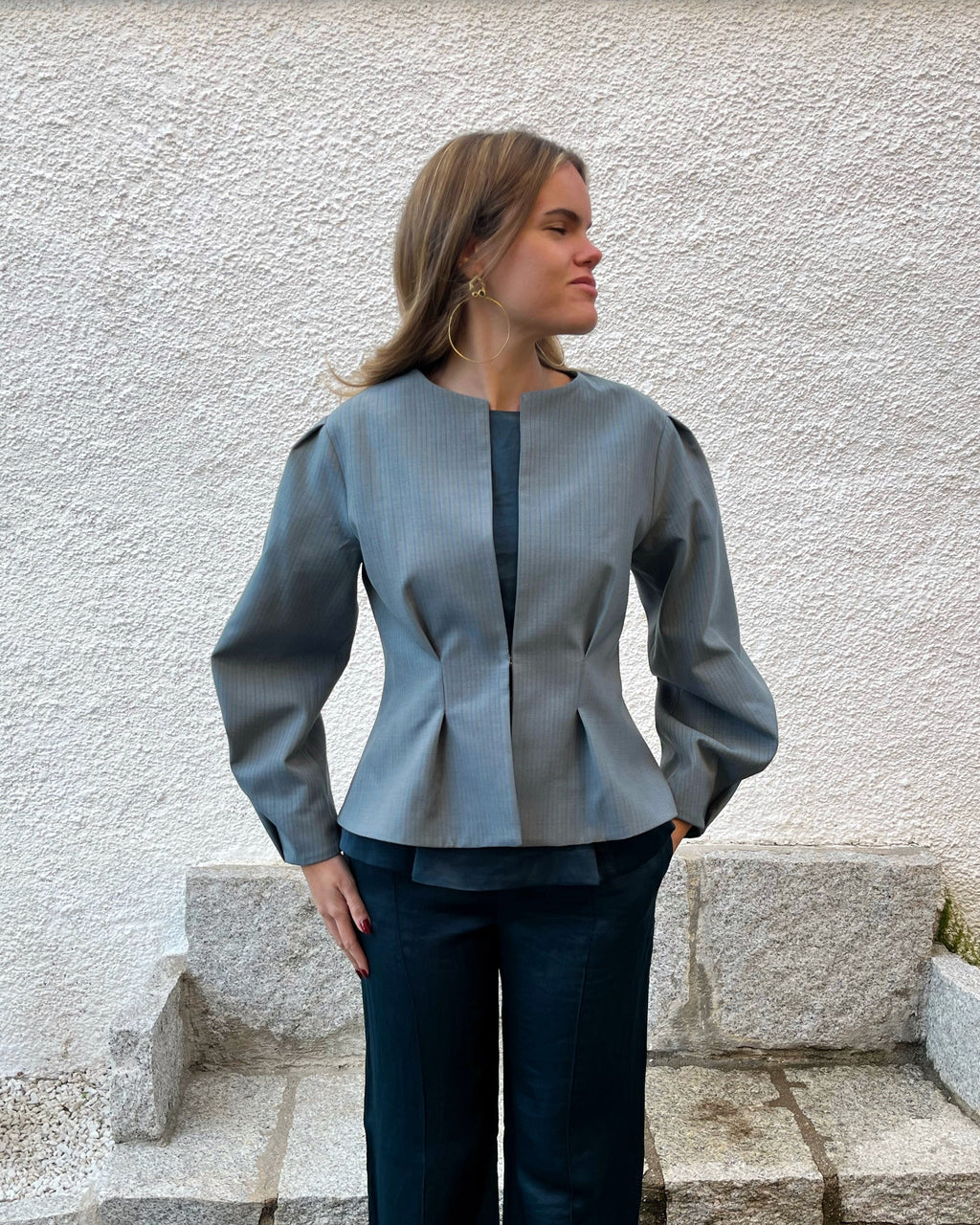 Chaqueta azul de mujer con rayas a tono y diseño elegante entallado; vista frontal con modelo en jardín, colección Historia de un sastre.