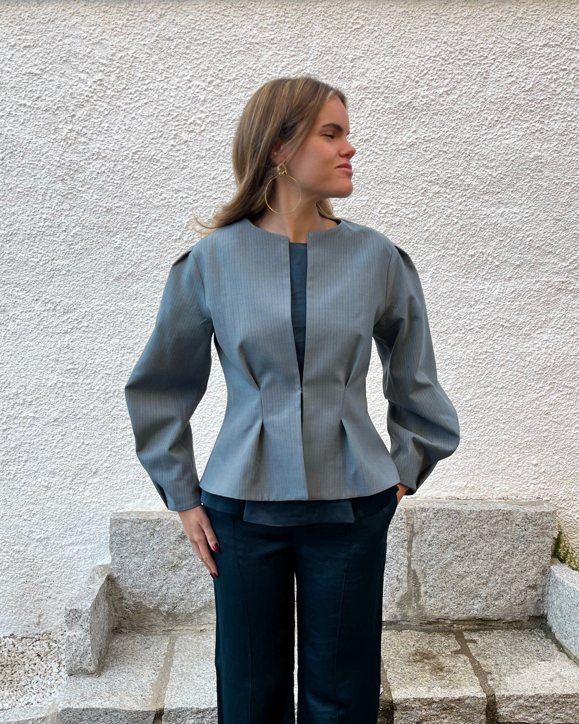 Chaqueta azul de mujer con rayas a tono y diseño elegante entallado; vista frontal con modelo en jardín, colección Historia de un sastre.