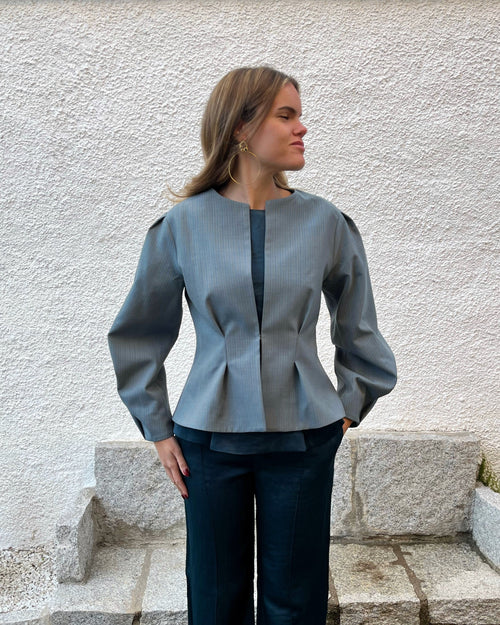 Chaqueta azul de mujer con rayas a tono y diseño elegante entallado; vista frontal con modelo en jardín, colección Historia de un sastre.