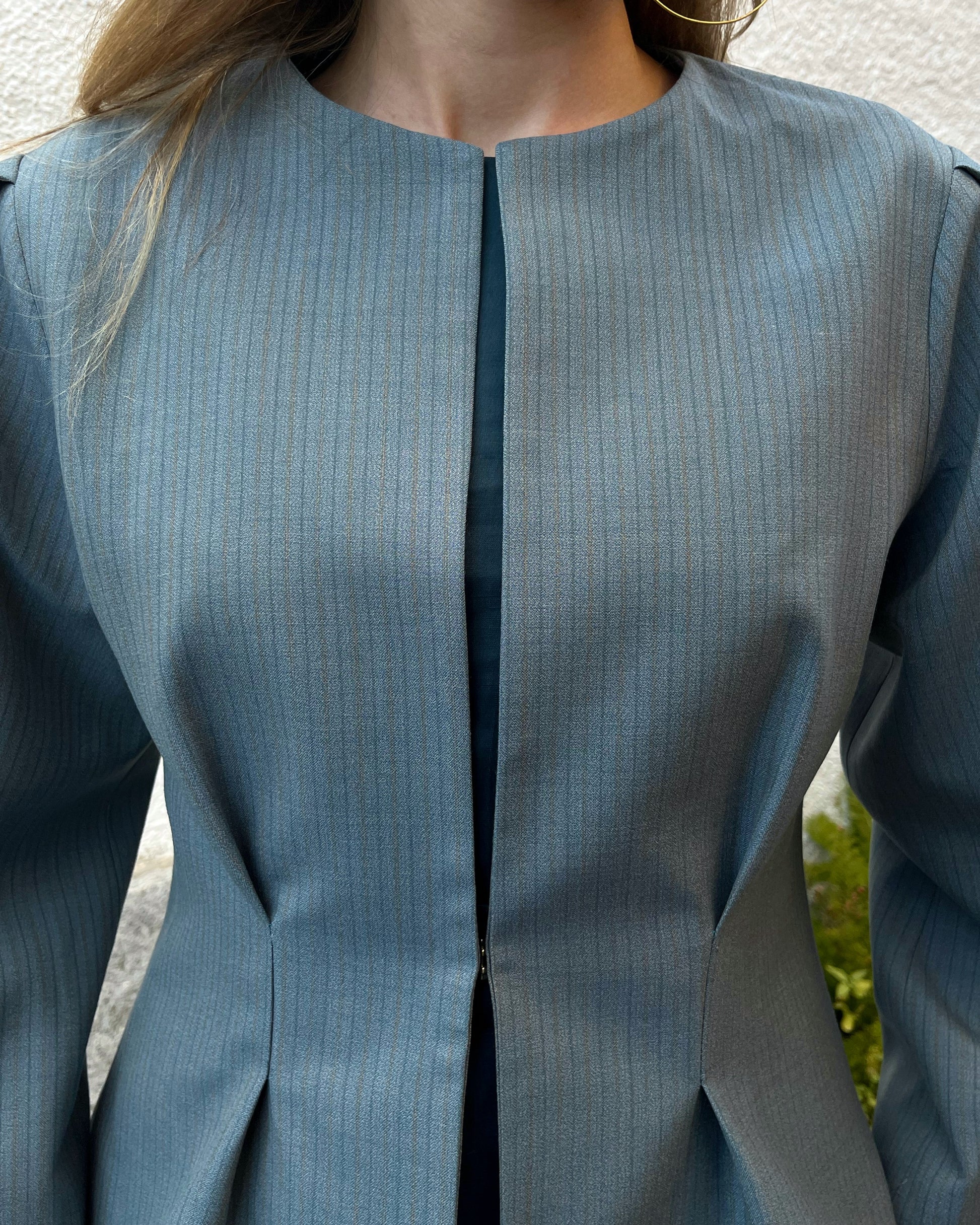 Detalle en zoom de chaqueta azul con rayas a tono y broche dorado oculto; diseño elegante de la colección Historia de un sastre.