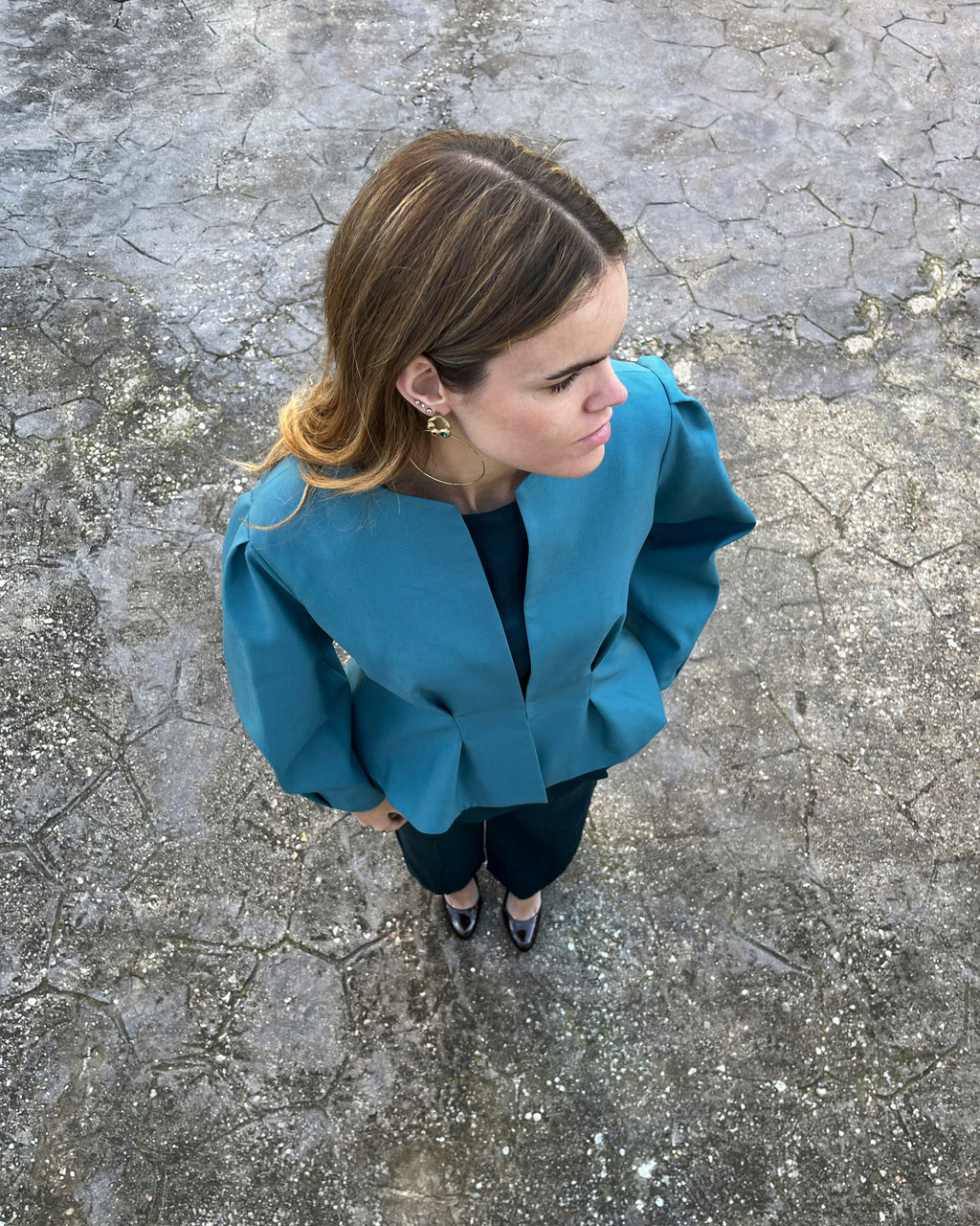 Vista cenital de chaqueta azul turquesa elegante de mujer con mangas abullonadas; modelo en jardín.