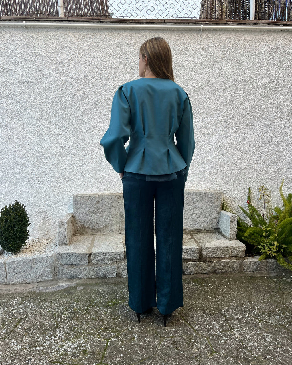 Chaqueta azul turquesa de mujer con corte entallado y pliegues traseros; estilo elegante en jardín.