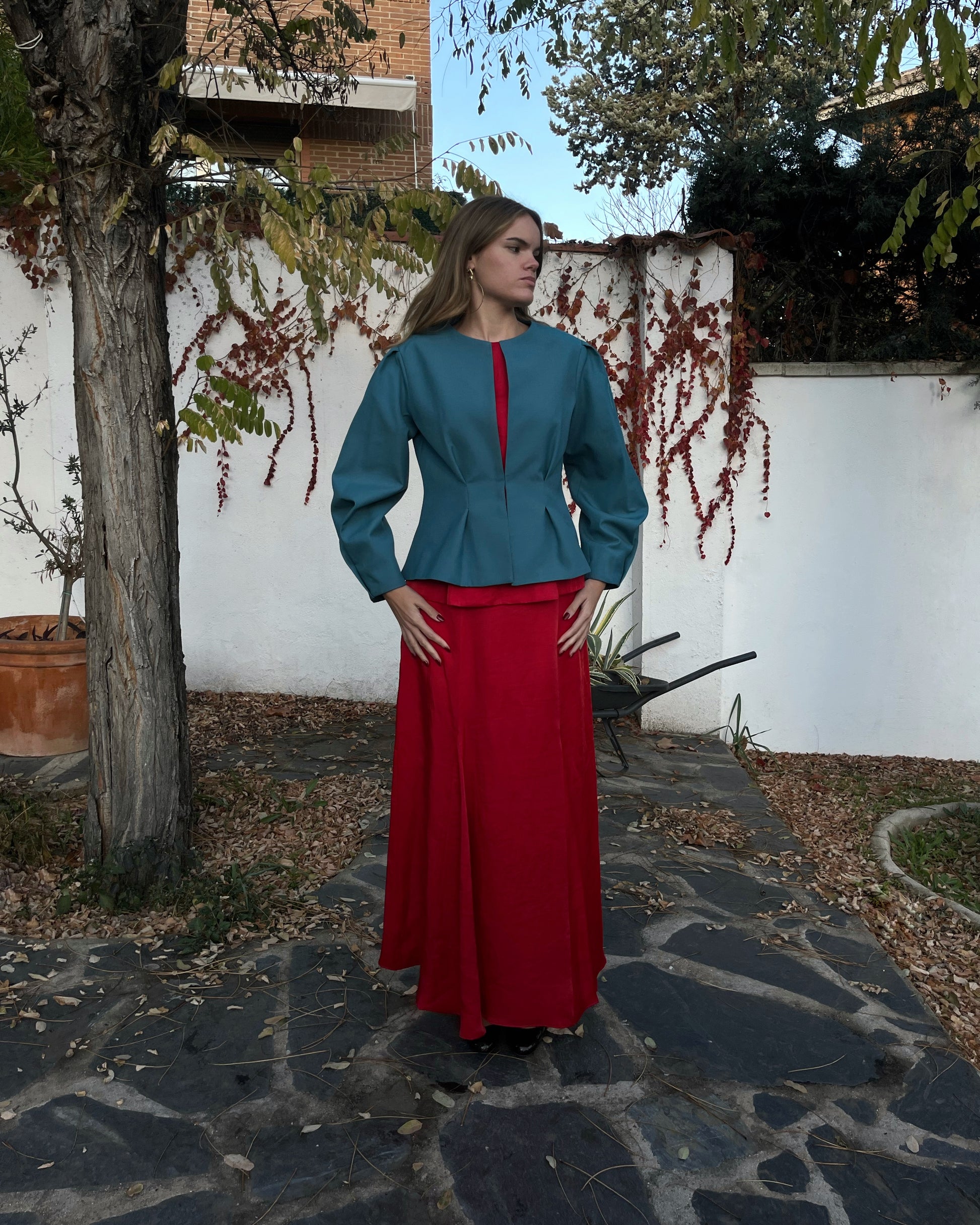 Chaqueta azul turquesa elegante de mujer con diseño entallado; vista frontal con modelo en jardín, colección Historia de un sastre.