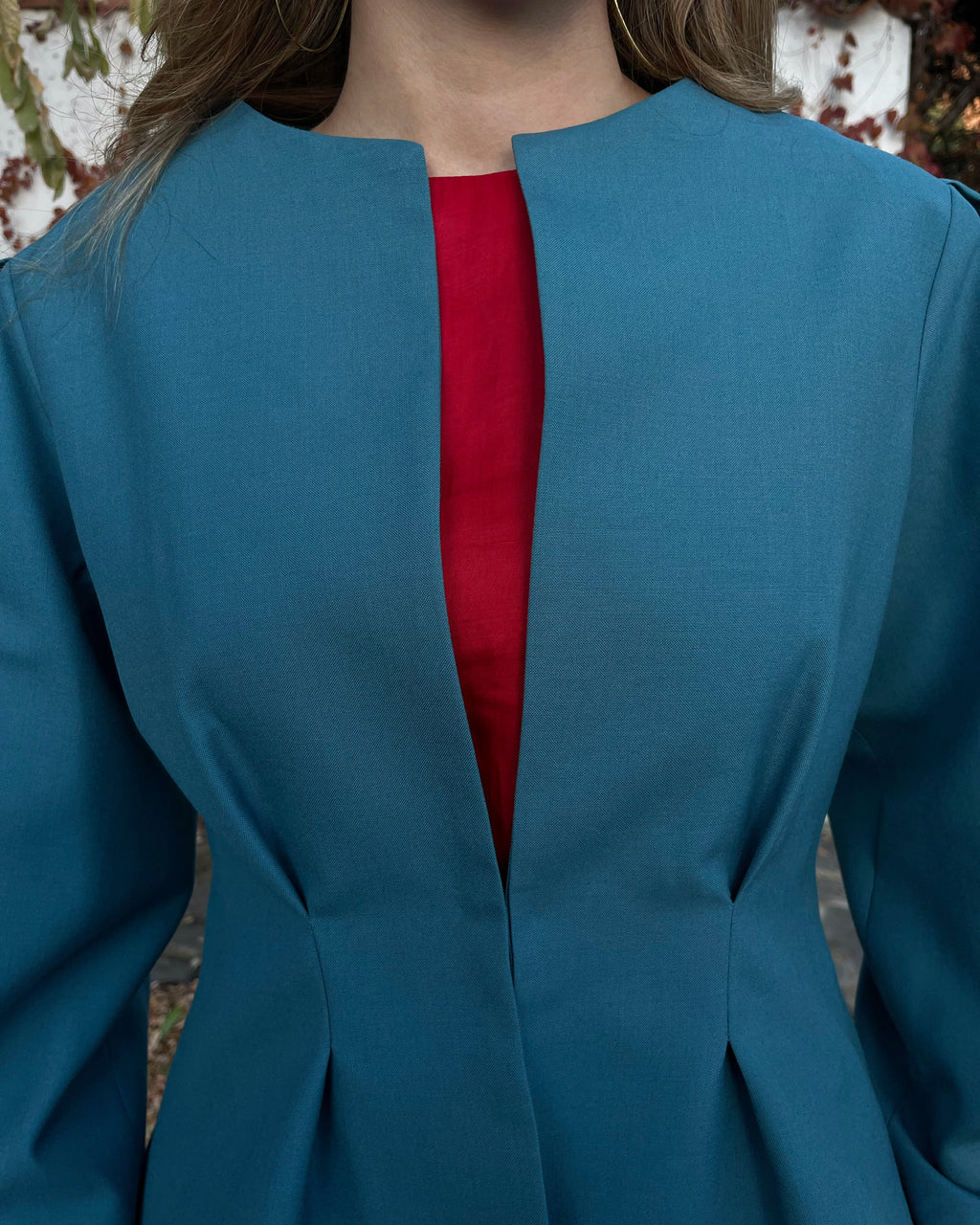 Detalle en zoom de chaqueta azul turquesa con broche dorado oculto; diseño elegante de la colección Historia de un sastre.