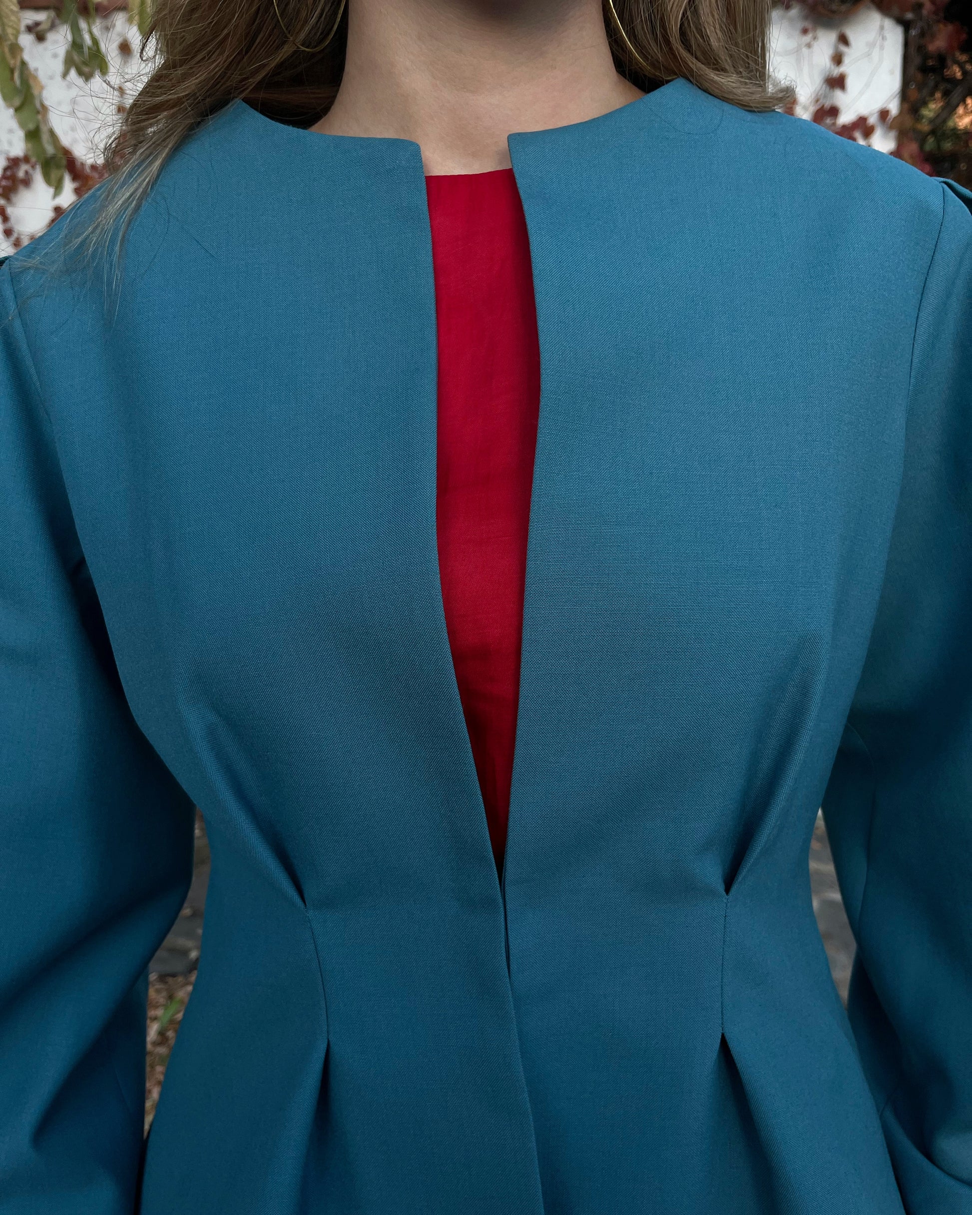 Detalle en zoom de chaqueta azul turquesa con broche dorado oculto; diseño elegante de la colección Historia de un sastre.