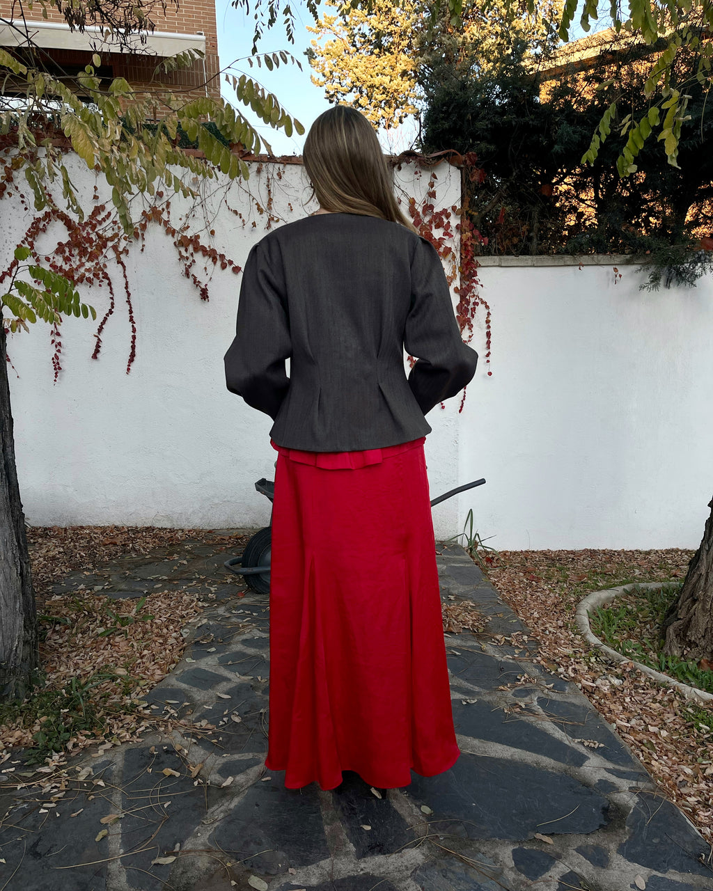 Chaqueta elegante de mujer con textura de espiga marrón y azul y corte entallado; vista trasera en jardín.