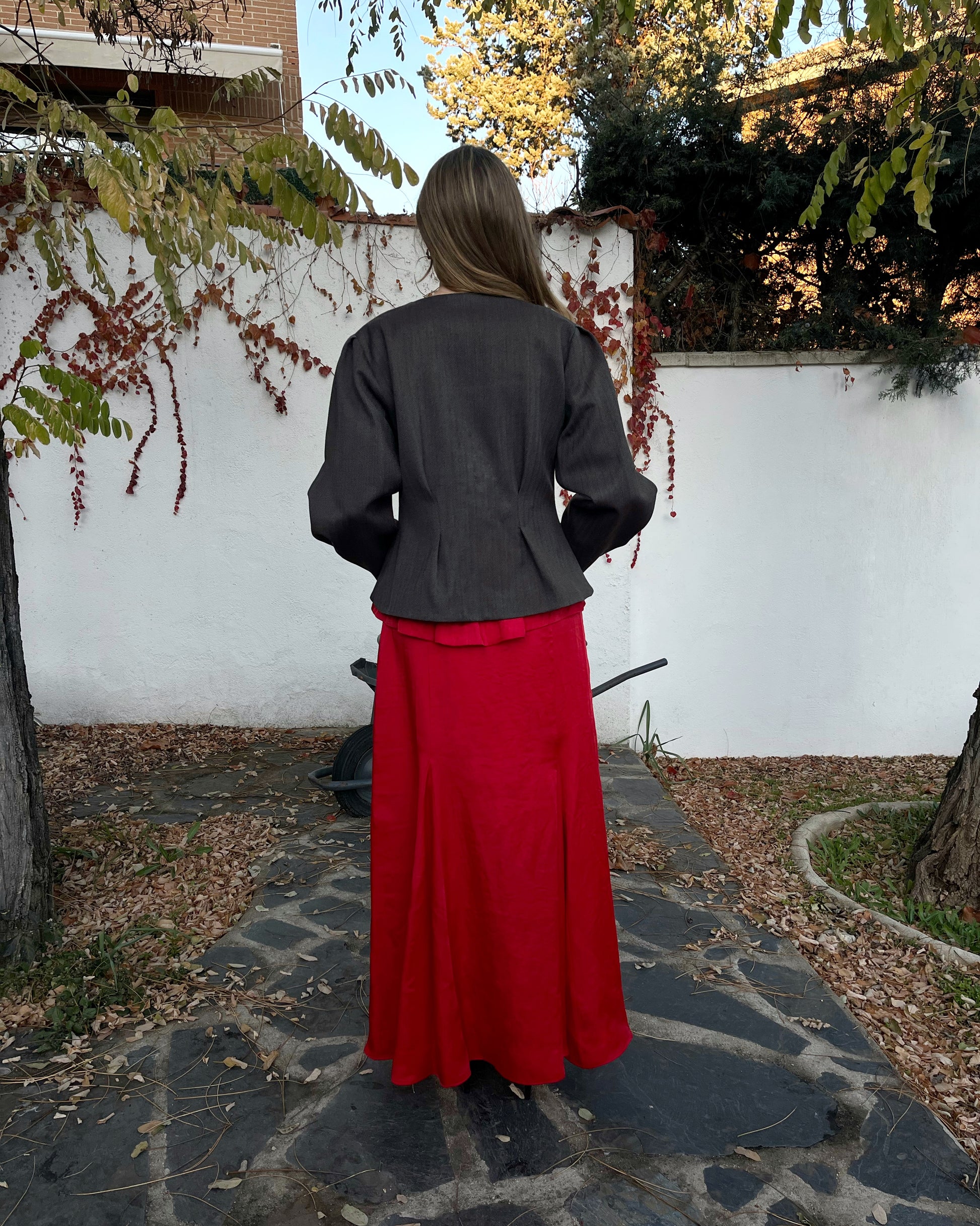 Chaqueta elegante de mujer con textura de espiga marrón y azul y corte entallado; vista trasera en jardín.
