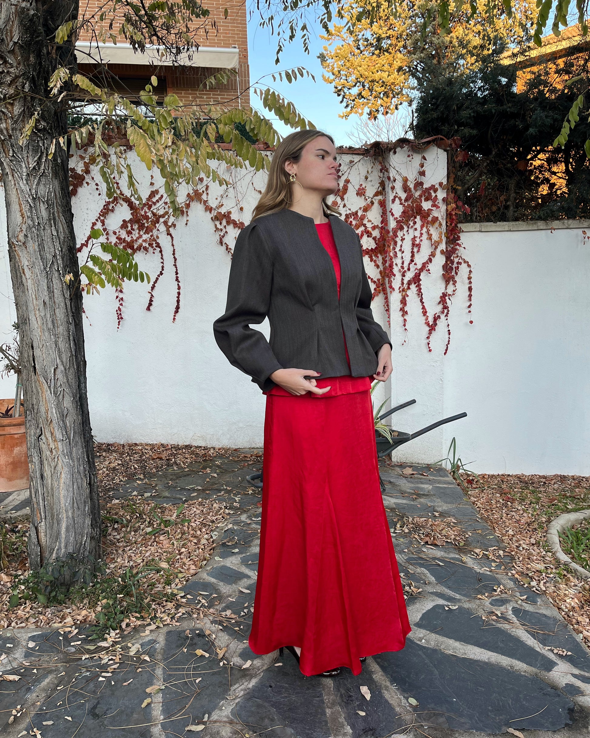 Vista lateral de chaqueta de espiga marrón y azul con mangas abullonadas y cierre oculto; modelo posando en jardín.