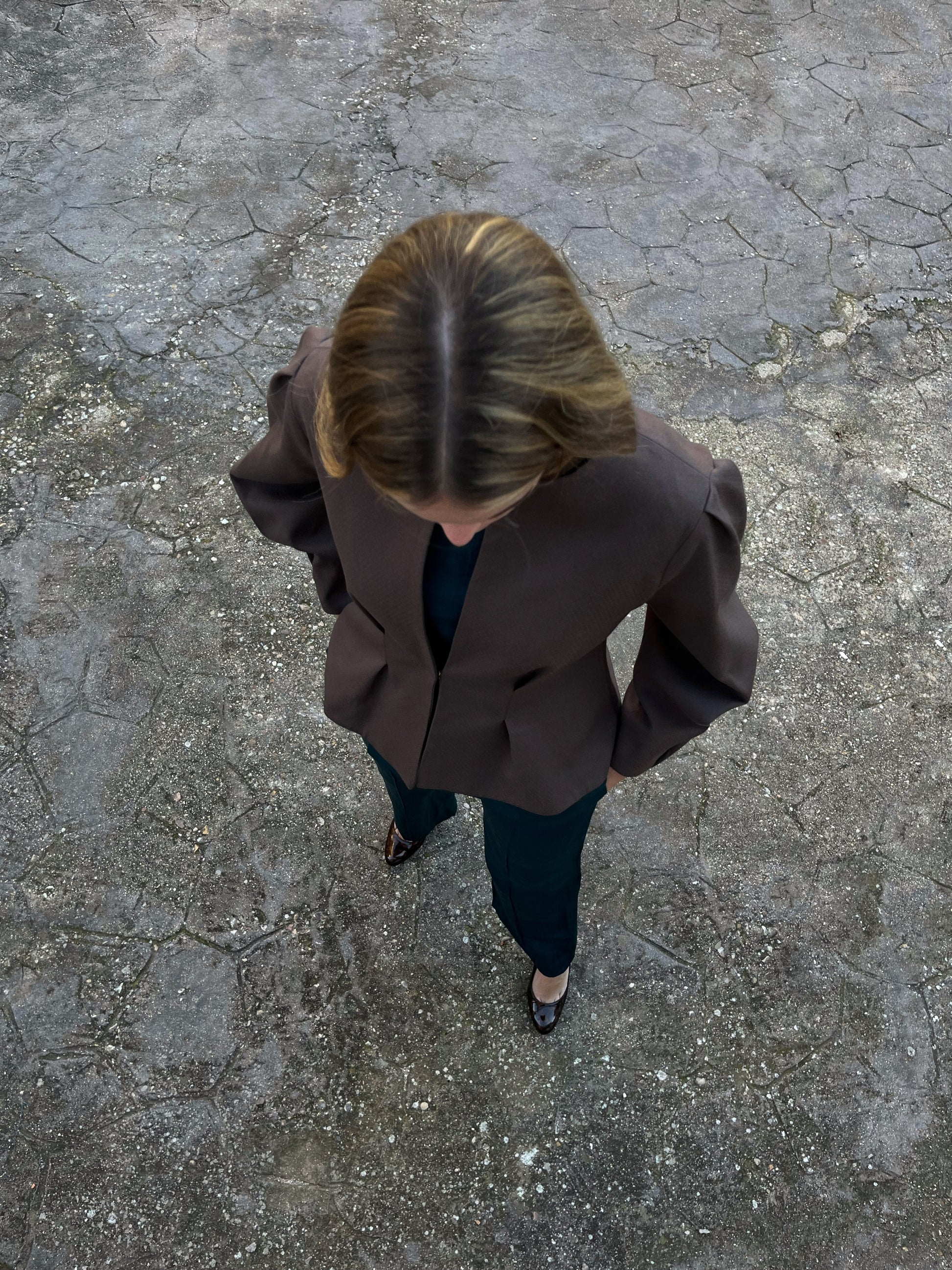 Vista cenital de chaqueta marrón elegante de mujer con textura de lunares y mangas abullonadas; modelo en jardín.