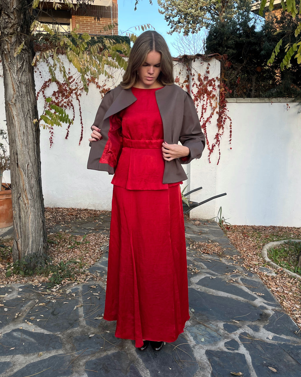 Detalle del forro rojo y exterior de la chaqueta marrón con textura de lunares; diseño elegante de mujer en jardín.