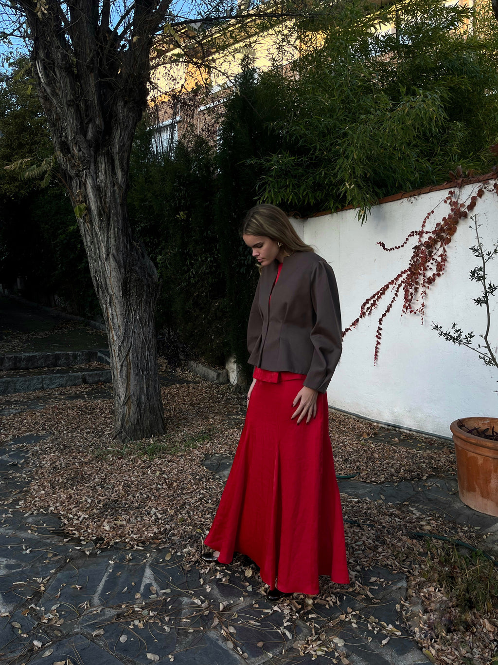 Vista lateral de chaqueta marrón elegante de mujer con textura de lunares y mangas abullonadas; modelo posando en jardín.