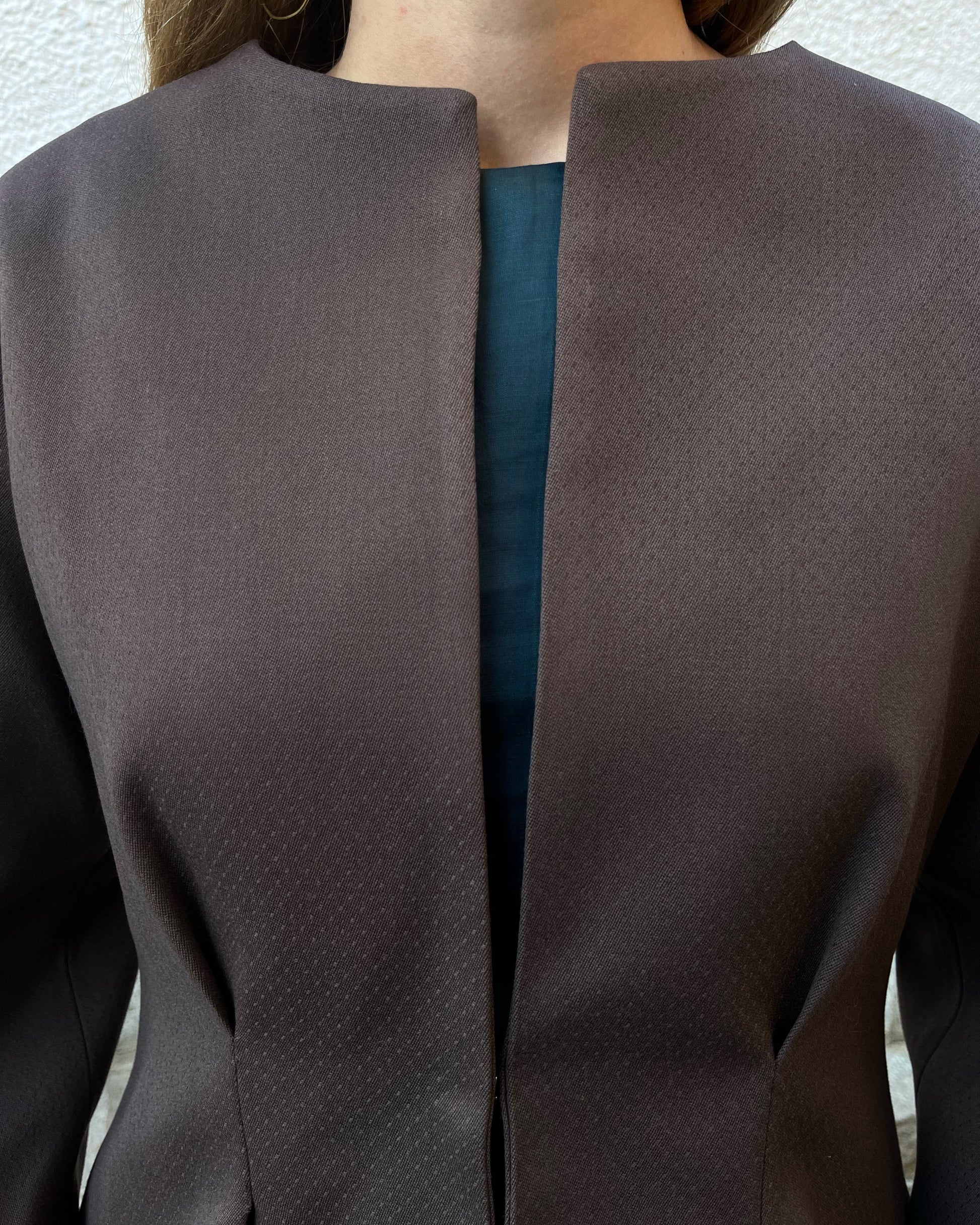 Detalle en zoom de chaqueta marrón de mujer con textura de lunares y broche dorado oculto; diseño elegante de la colección Historia de un sastre.