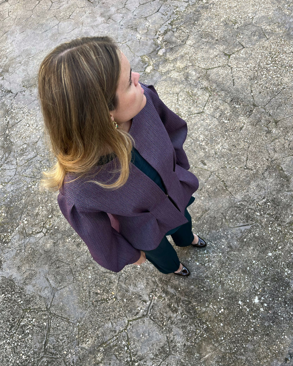 Vista cenital de chaqueta morada elegante de mujer con textura de espiga; modelo en jardín.