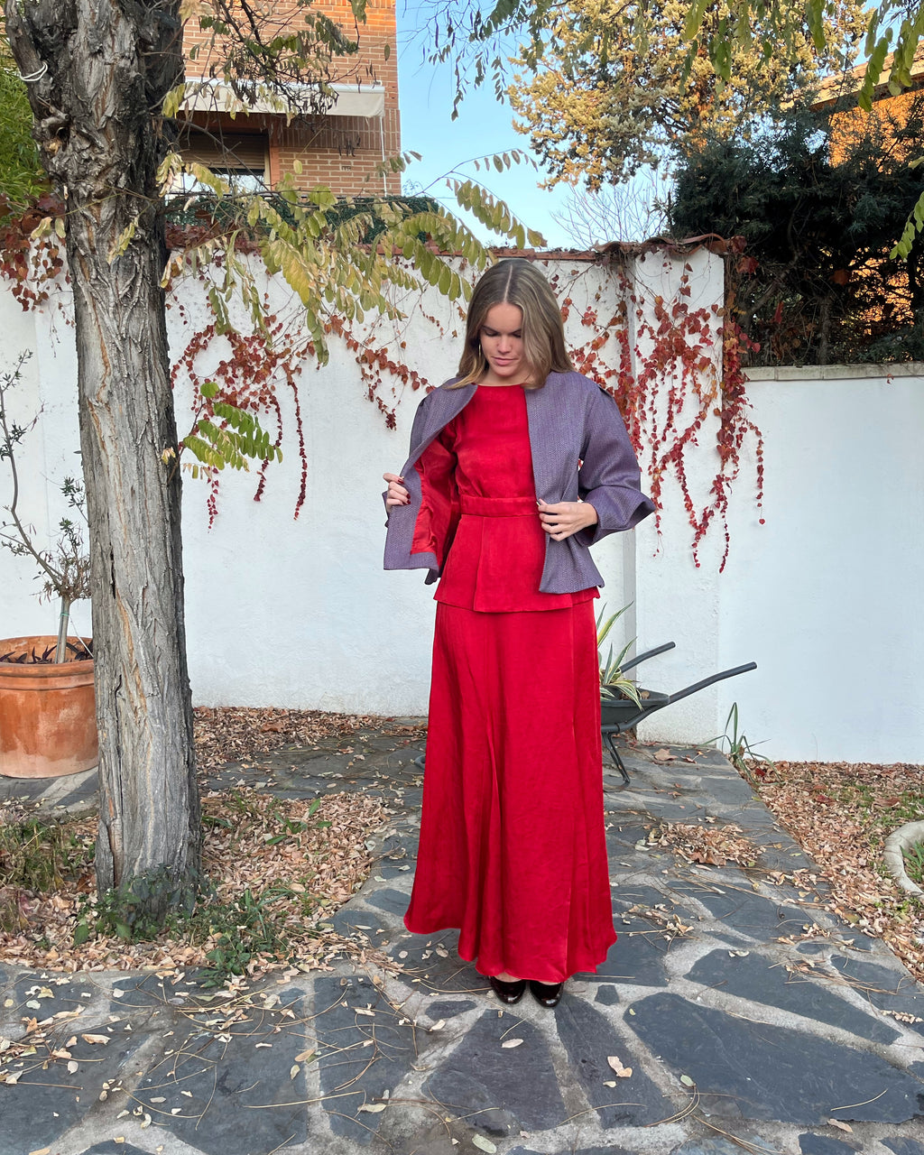 Detalle del forro rojo y exterior de la chaqueta morada con textura de espiga; diseño elegante para mujer en jardín.
