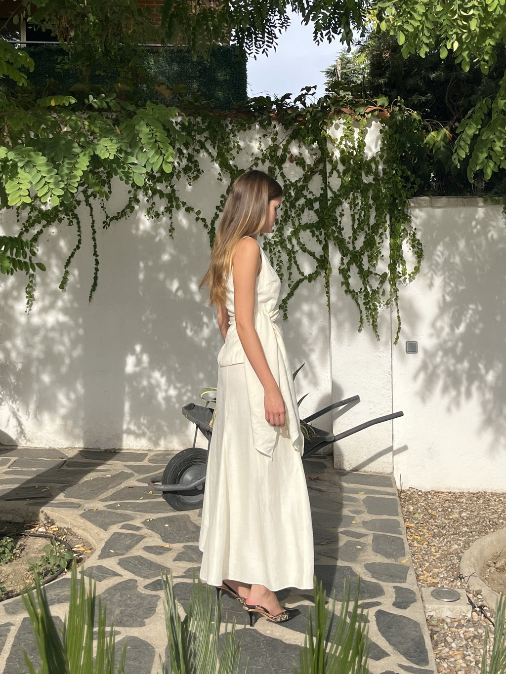  Vista lateral del conjunto blanco crudo de top con lazo y falda larga de godets, resaltando su movimiento y elegancia en cada detalle