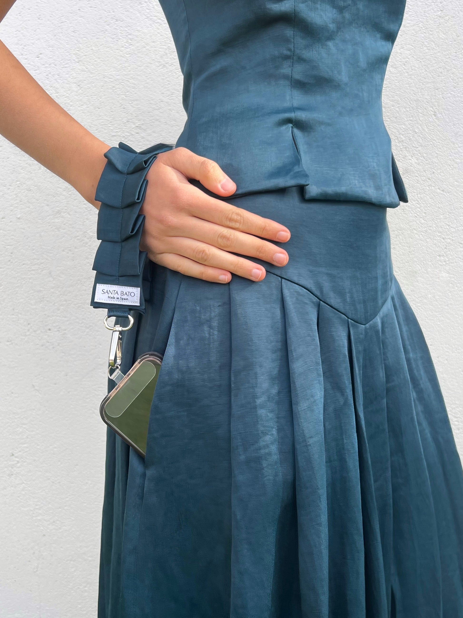 Mujer guardando móvil con correa azul plisada, accesorio práctico y elegante para mujer