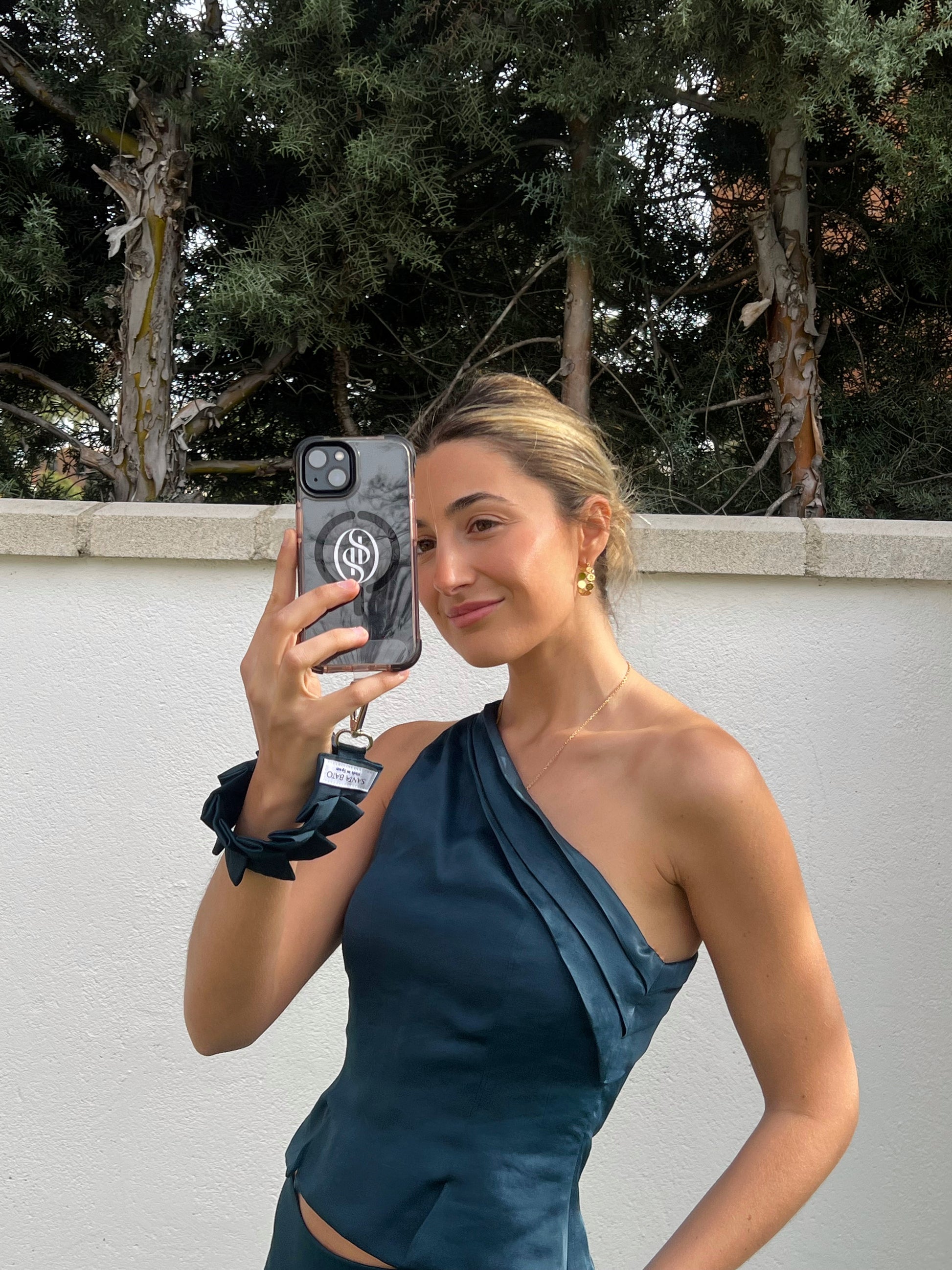 Mujer tomando foto con móvil sujeto a correa azul plisada, accesorio de moda elegante para eventos