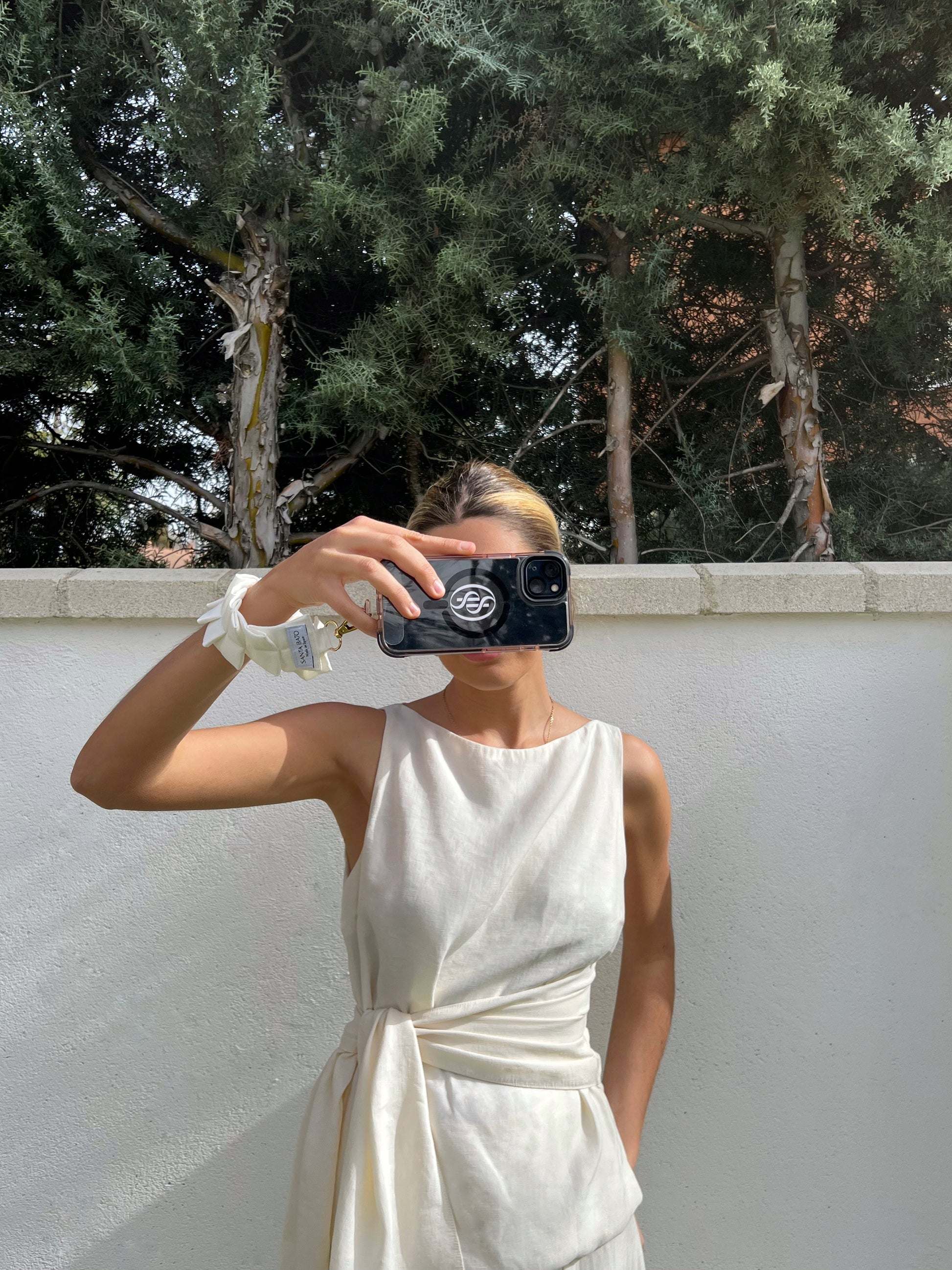 Mujer tomando foto con móvil sujeto a correa blanca plisada, accesorio de moda para eventos