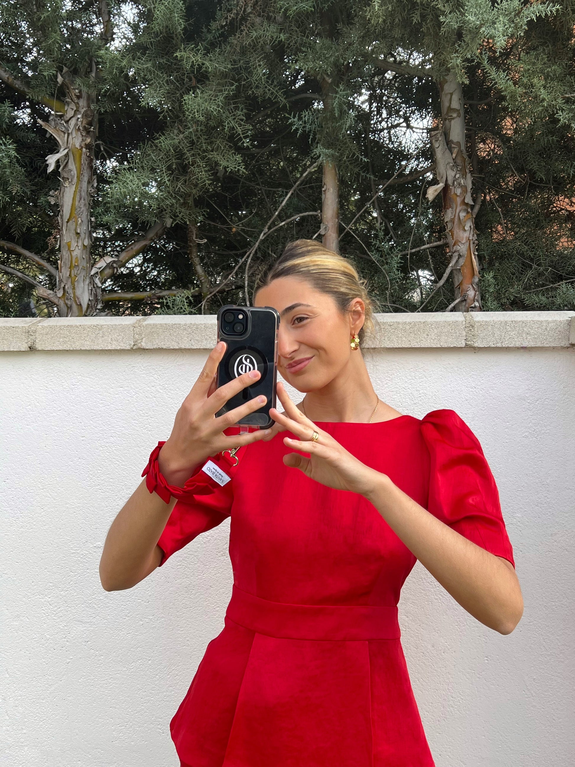 Mujer tomando foto con móvil sujeto a correa roja plisada, accesorio elegante para eventos