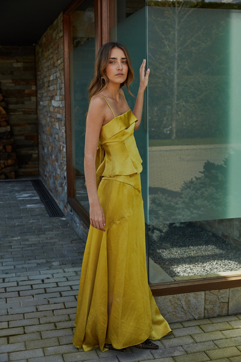 Vista lateral de falda color aceite amarillo verde dorado elegante de mujer con godets y caída fluida que aporta movimiento al caminar; modelo en jardín.