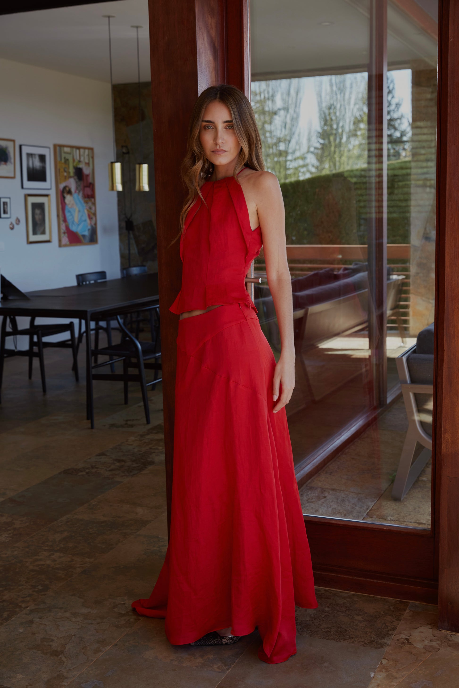 Vista lateral de falda rojo elegante de mujer con godets y caída fluida que aporta movimiento al caminar; modelo en jardín.