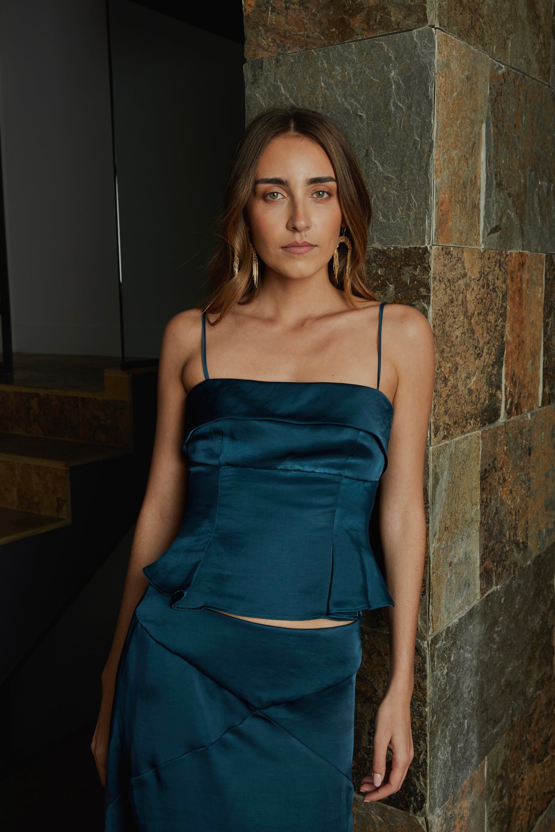 Top azul petróleo de mujer con tirantes finos y escote recto, diseño elegante ideal para invitada; vista frontal con modelo en jardín.