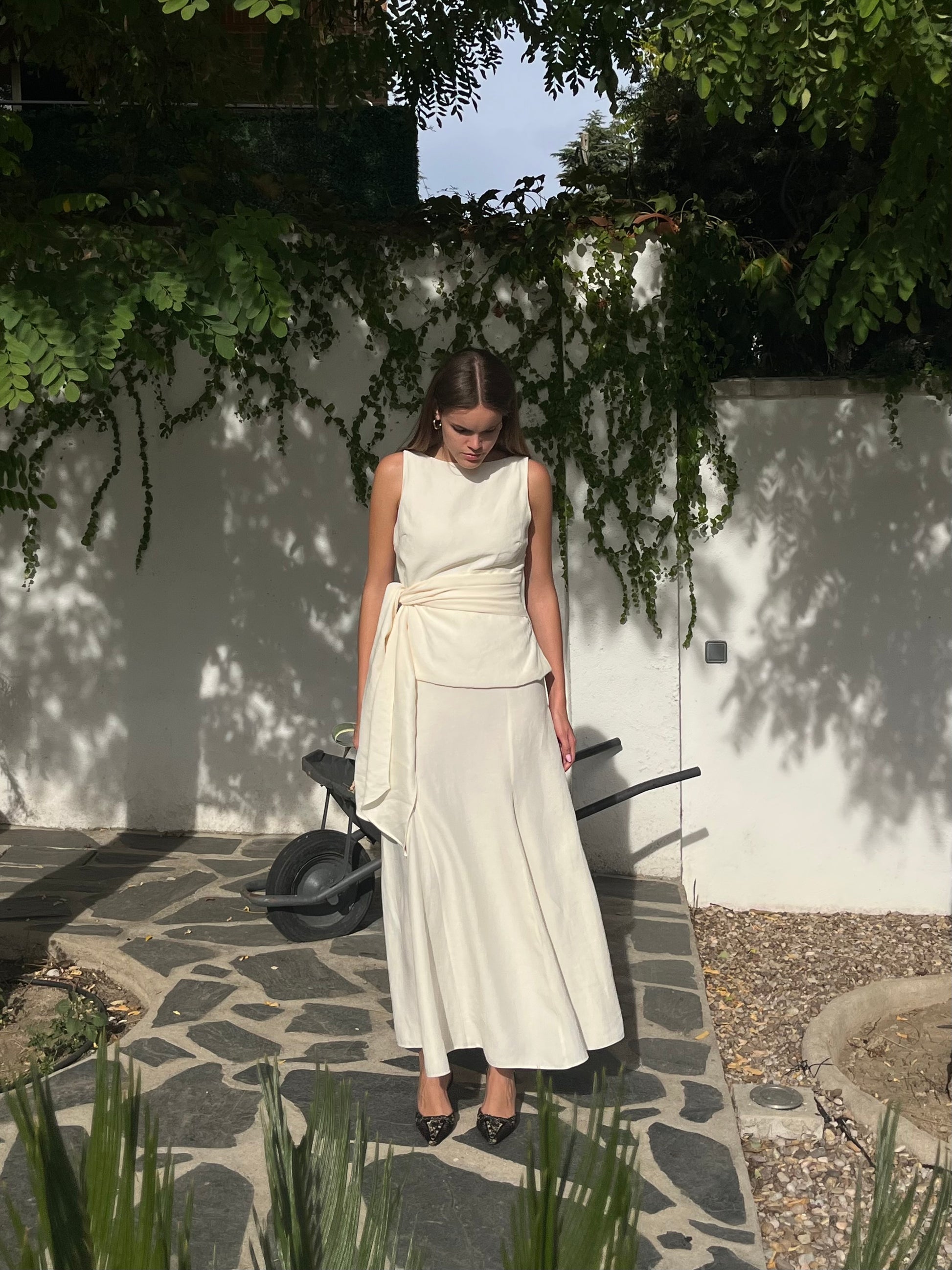 lismo completo en blanco crudo de top con lazo y falda larga de godets, pensado para invitadas que buscan un look elegante y atemporal en bodas o prebodas