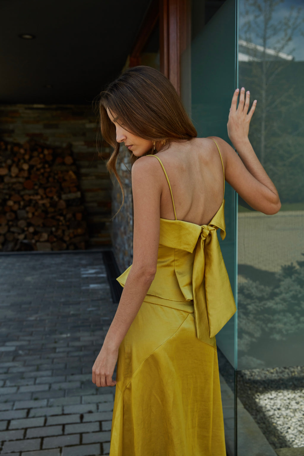 Vista trasera de top color aceite amarillo verde dorado elegante de mujer con tirantes finos y lazo en la espalda; diseño ideal para eventos y bodas en jardín.