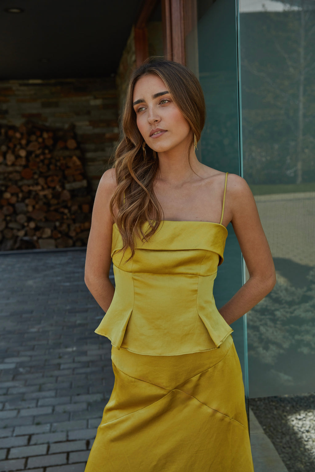 Top color aceite amarillo verde dorado de mujer con tirantes finos y escote recto, diseño elegante ideal para invitada; vista frontal con modelo en jardín.