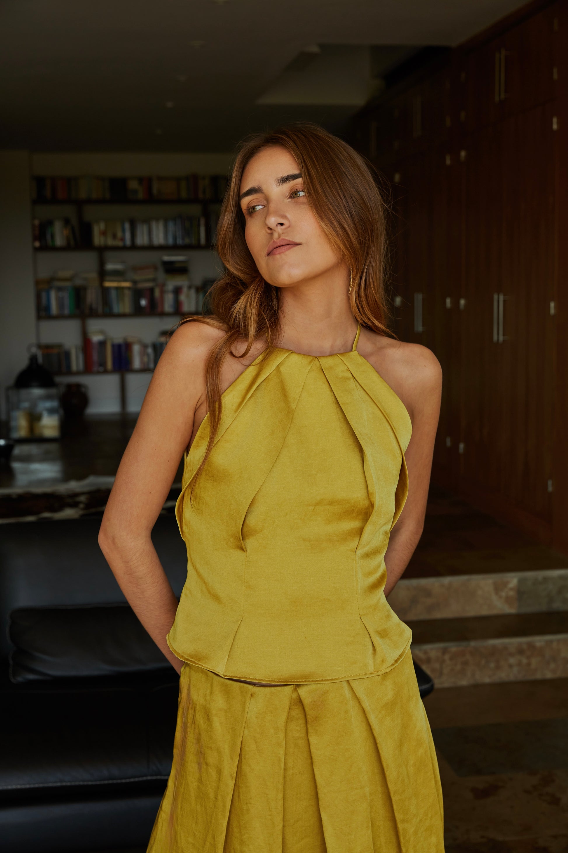 Top halter color aceite amarillo verde dorado plisado elegante de mujer con tejido efecto lino y caída estructurada; vista frontal con modelo en jardín.