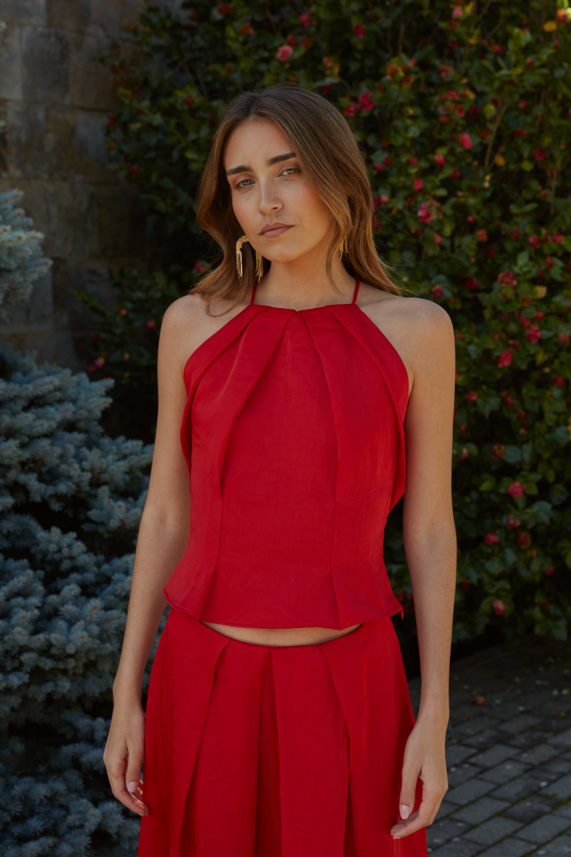 Top halter rojo plisado elegante de mujer con tejido efecto lino y caída estructurada; vista frontal con modelo en jardín.