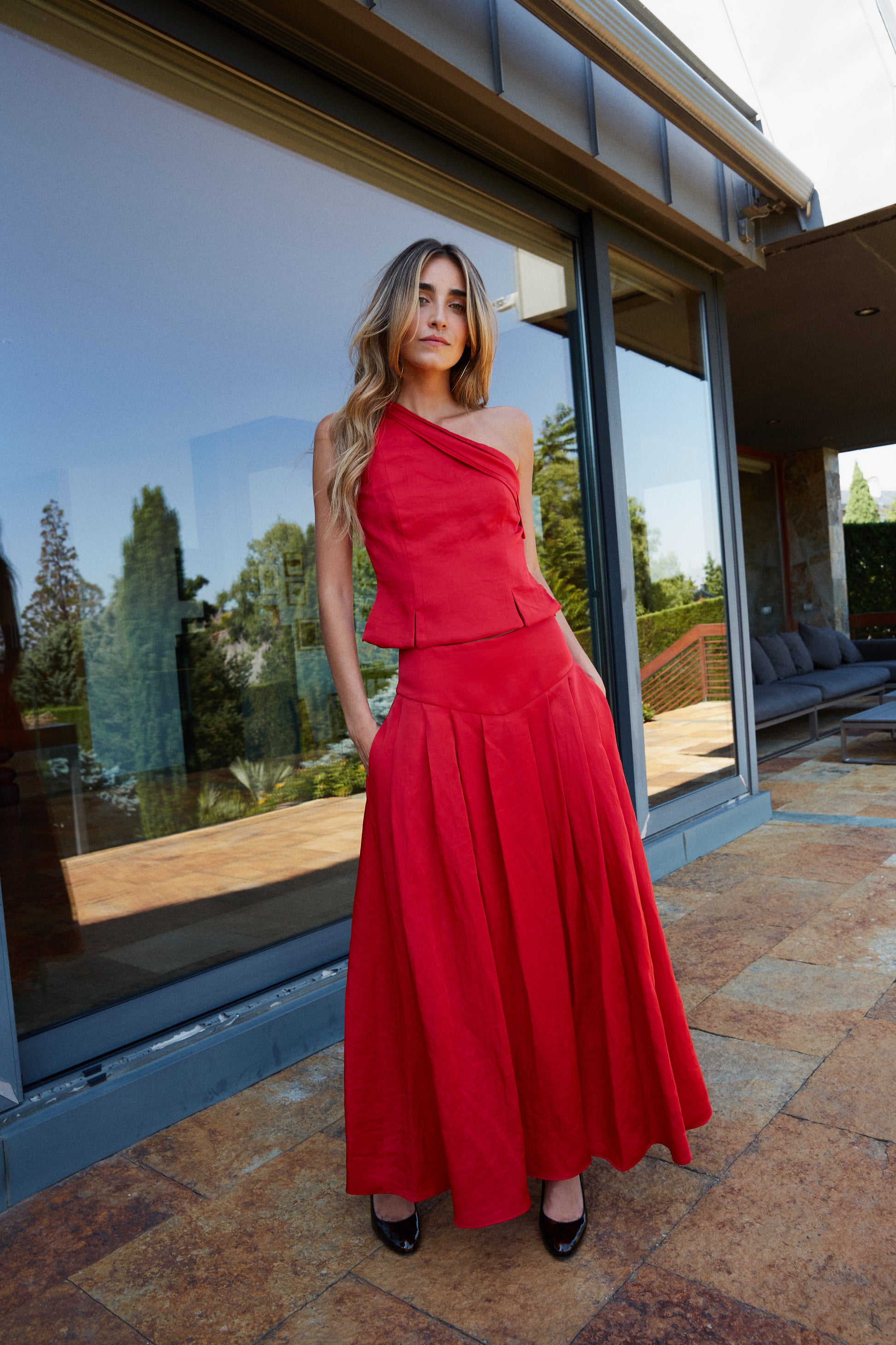 Top rojo con escote asimétrico combinado con falda de tablas, conjunto sofisticado.