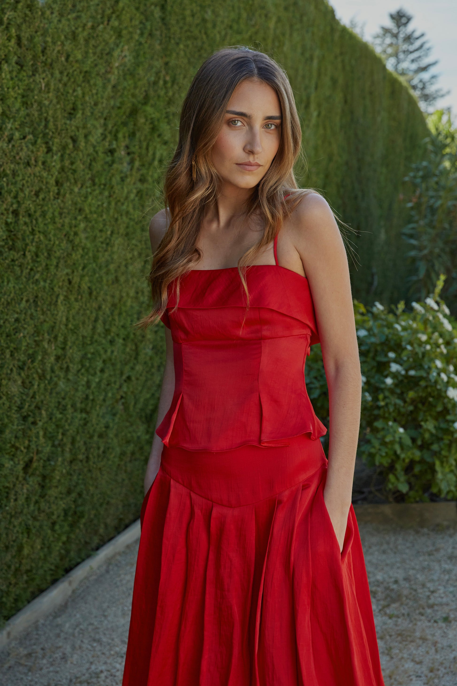 Top rojo de mujer con tirantes finos y escote recto, diseño elegante ideal para invitada; vista frontal con modelo en jardín.